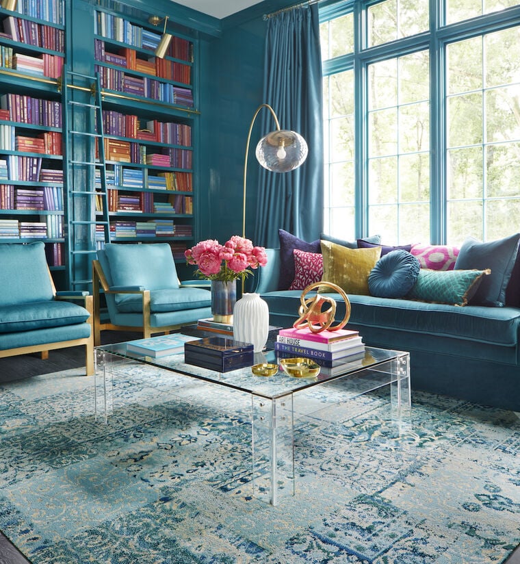 FLOR Reoriented living room rug in Teal with teal and wood couch and chairs and glass table.